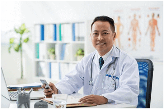 A doctor sitting at his desk with a cell phone.