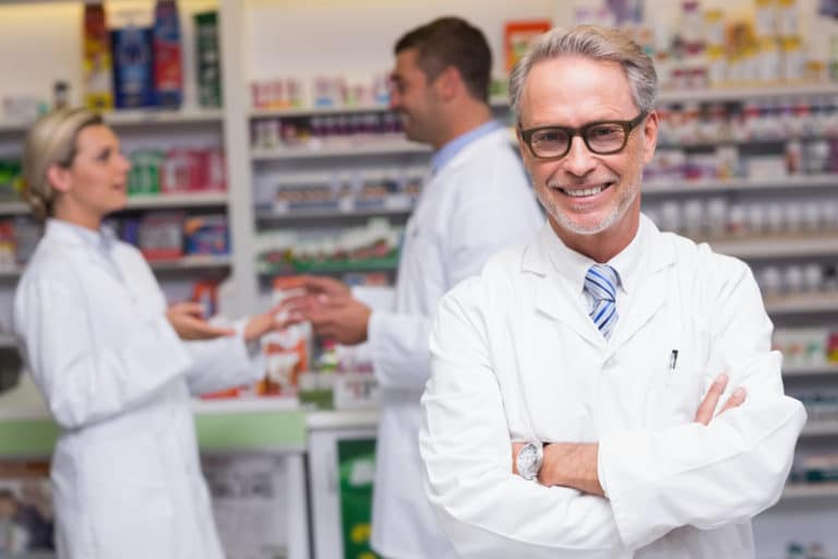 A man in white lab coat standing next to other pharmacists.