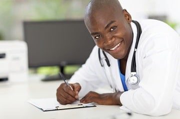 A doctor is smiling while writing on paper.