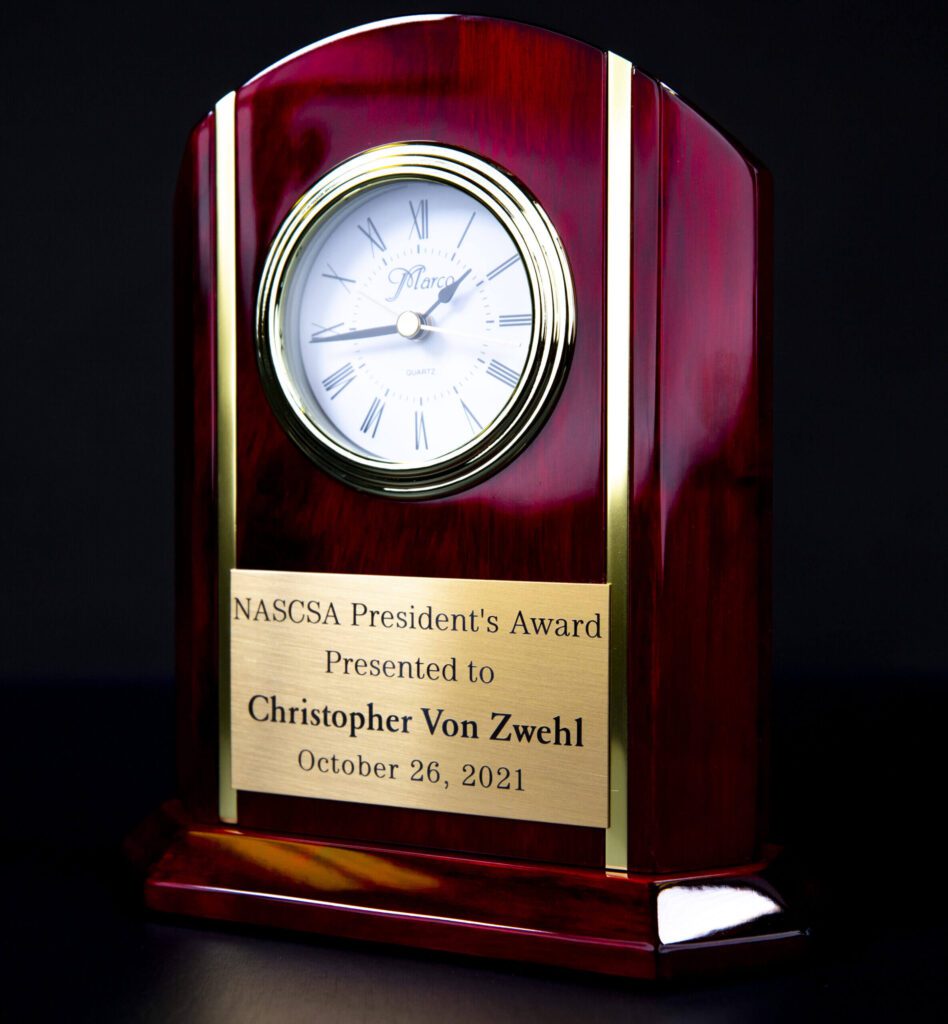 A wooden clock with a plaque on top of it.