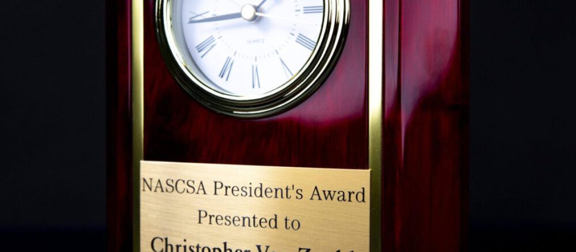 A wooden clock with a plaque on top of it.